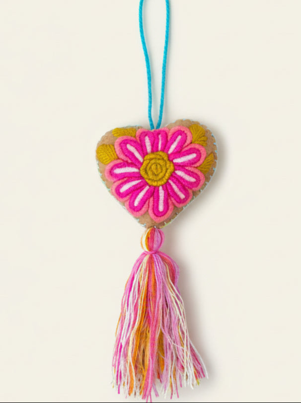 Heart-shaped decorative item with a pink flower design and colorful tassel on a dark background
