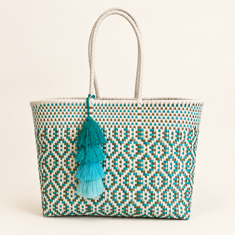 A woven tote bag with a geometric pattern in teal, white, and brown, featuring white rope handles and a tiered turquoise tassel charm.
