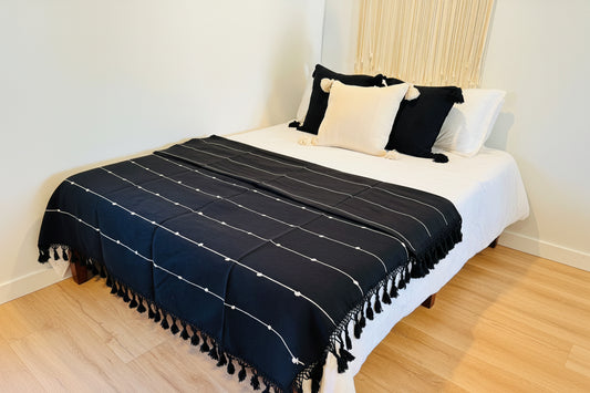 Black tassel blanket on a bed with white pillows in a room.
