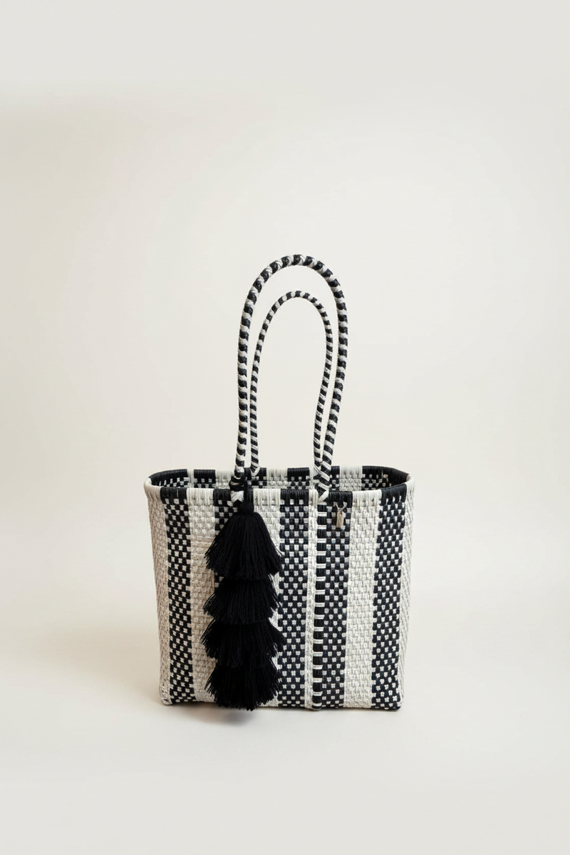 Black and white woven tote bag with tassels on a light background