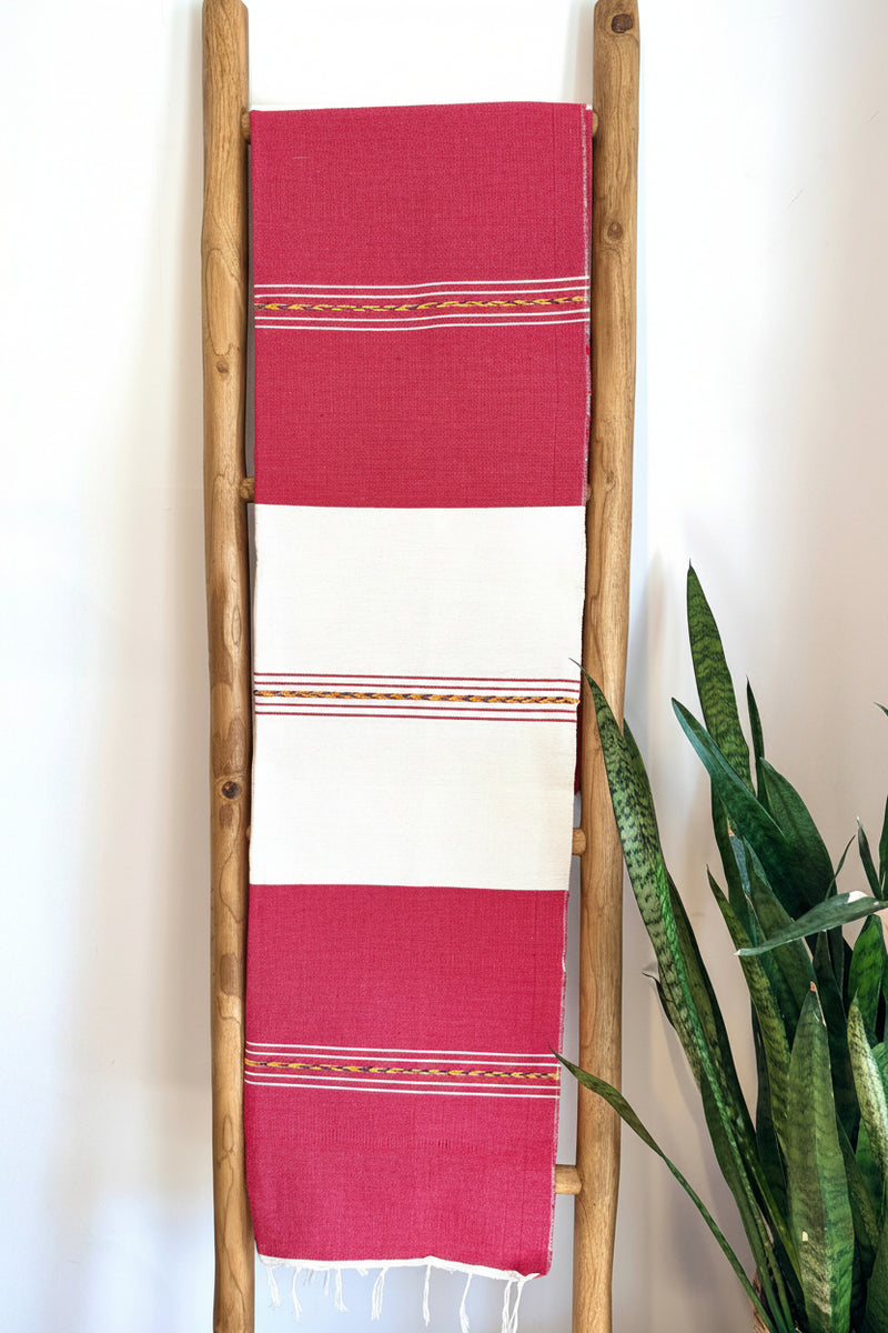 A red and white striped handwoven Mexican throw blanket draped over a wooden ladder, with a green plant in the background.