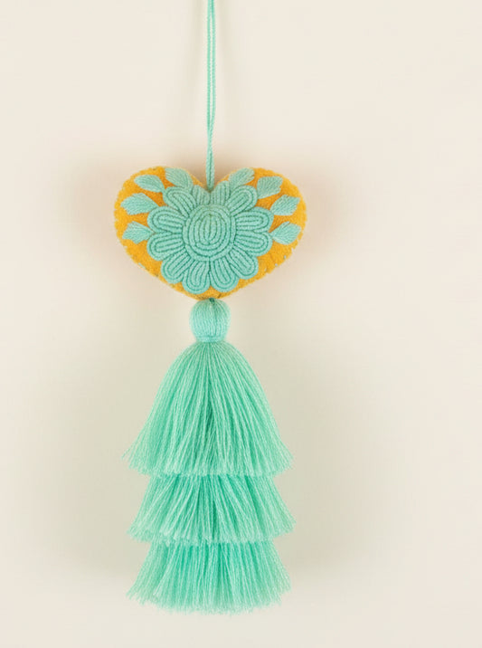 Decorative heart-shaped tassel with green and orange colors on a dark background