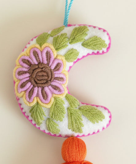 Decorative crescent moon with floral embroidery and tassel on a dark background