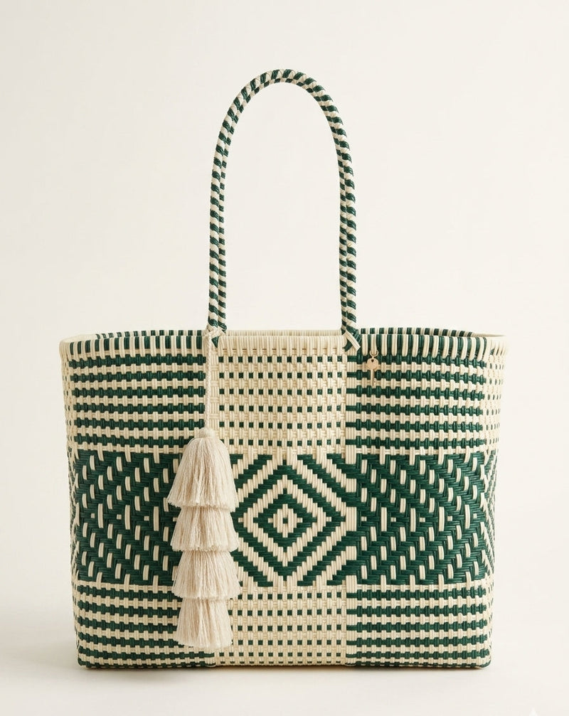 A woven tote bag with a geometric pattern in dark green and cream, featuring two braided shoulder straps and a decorative cream tassel, set against a plain off-white background.